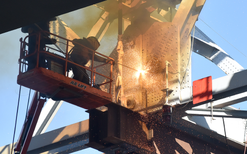 Man cutting metal bridge component.
